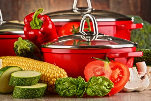 Composition with red steel pots and variety of fresh vegetables.