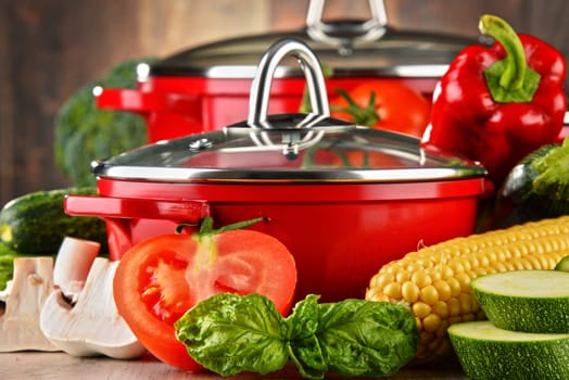Composition with red steel pots and variety of fresh vegetables.