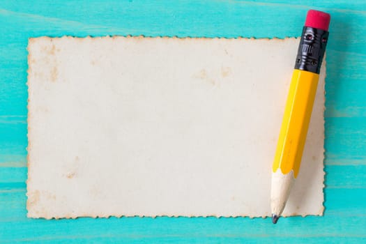 Yellow pencil with old paper on the blue wood surface