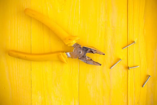 Pliers and few nails on the yellow wood surface