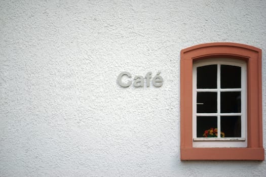 The facade of a coarse-grained plastered café with a small window in which stands a flower vase.