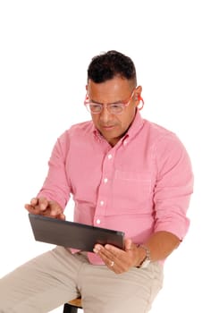 A middle age Hispanic man sitting on a chair, working on his tablet .computer, with safety glasses and earplug's, isolated for white background..
