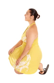 A lovely young woman in a yellow dress and sandals, kneeling on the.floor, isolated for white background..