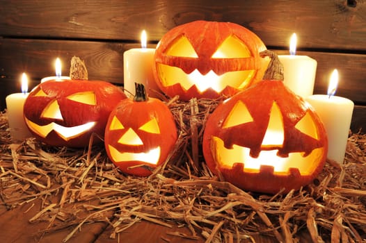 Three illuminated Halloween pumpkins with straw on old weathered wooden boards against a red-brown background in red light
