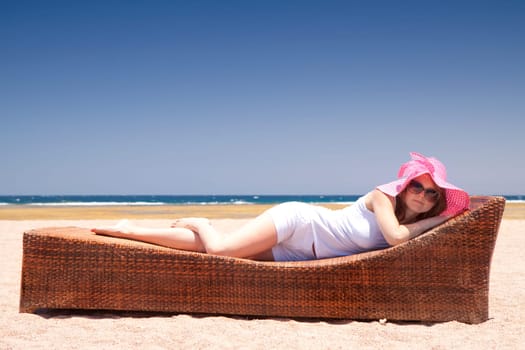 Pretty woman in a hat relaxes on a lounger on the beach.