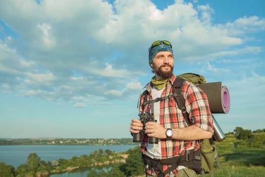 Young smilimg caucasian tourist with backpack  standing on the top of hill. The concept of an invitation to travel
