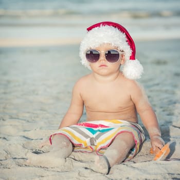 Cute baby wearing Santa hat on the beach