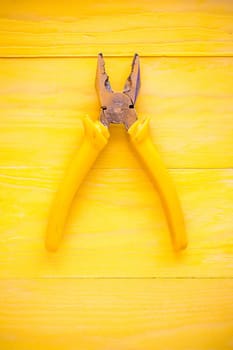 Old pliers on the yellow wooden surface