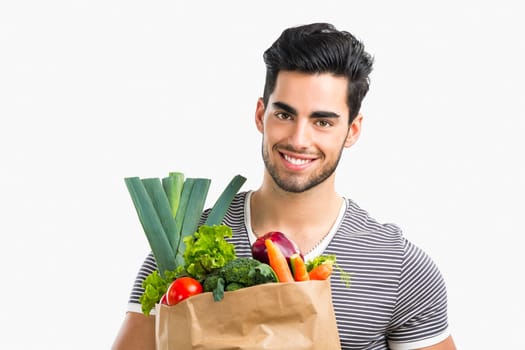 Handsome young man carrying a bag full of vegetables, isolated over white background