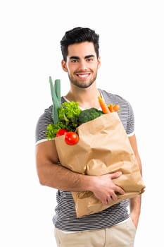 Handsome young man carrying a bag full of vegetables, isolated over white background
