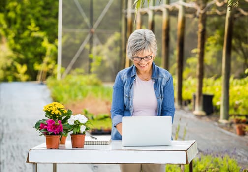 Beautiful mature woman working in a greenhouse holding flowers on her hands