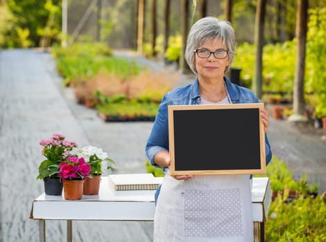 Beautiful mature woman working in a greenhouse holding flowers on her hands