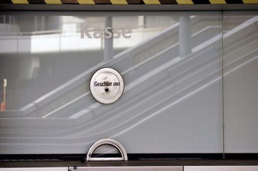 A cash register with reflections of an escalator in the window pane of the ticket office.