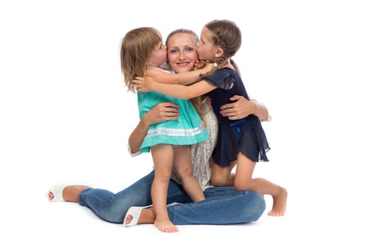Two little daughters kiss Mom in the studio on a white background.