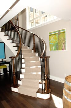 A round staircase to the basement bar in a new house with hardwood.floor and a beer barrel in the foreground..