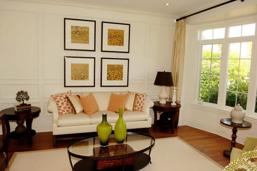 A nice living room with a large window, sofa and chairs with pictures on.the wall and an glass table in a new house..