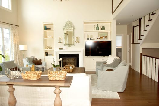 A luxurious living room with a fireplace and flat television, sofa and table,.with a staircase in the background and big window's..