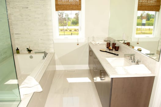An elegant bright lit bathroom with a sink and bathtub and a window.and marble floor..