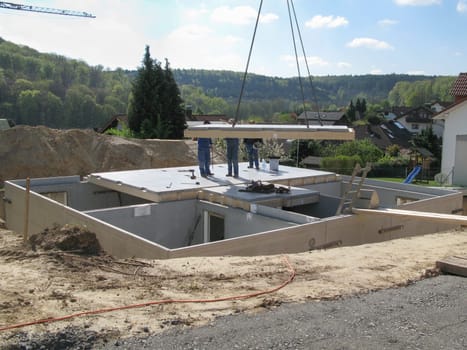 Three construction workers place a floor slab hanging from the crane on a prefabricated cellar