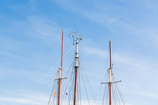 Various ship masts in a marina in Holland,in front of a bright blue sky.