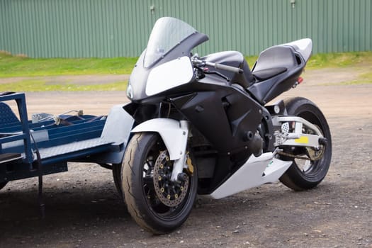 A modern racing superbike leaning against its trailer in the paddock at a racetrack.