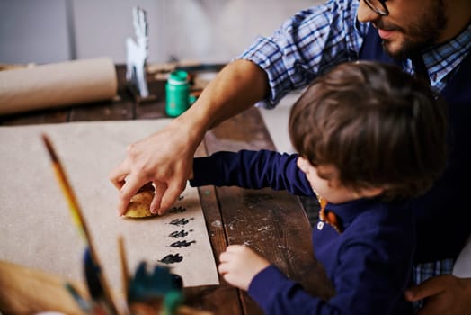 Young man and his son printing firtree shapes on paper