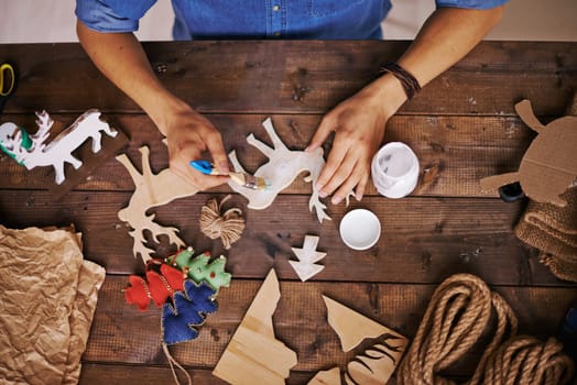 Male hands painting wooden toy deer with white gouache