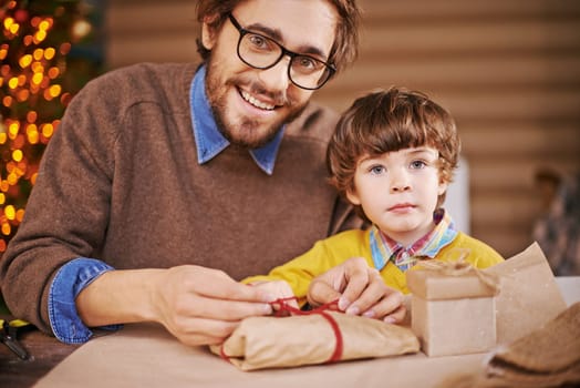 Young man packing xmas gift and looking at camera with his son near by