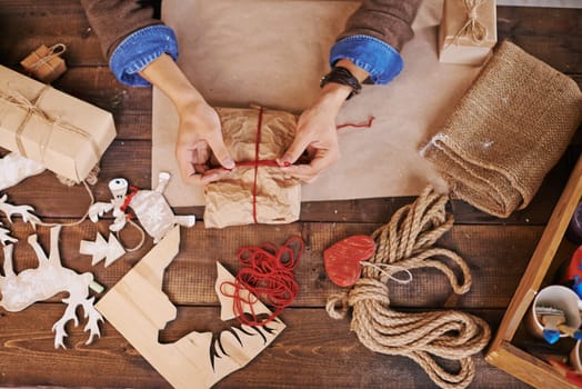 Hands of young man tying up wrapped xmas gift with red thread