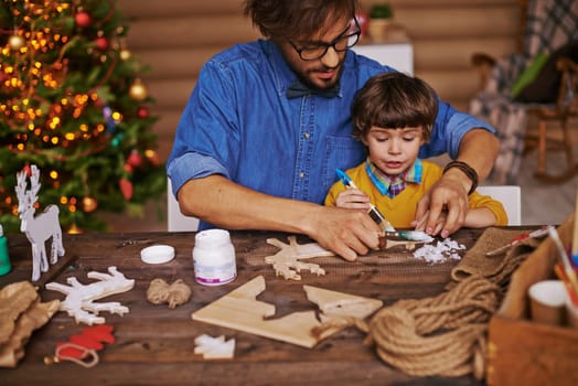 Young man showing his little son how to paint wooden xmas toys