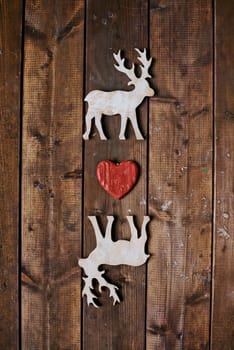 Two reindeers with red heart between them on wooden background