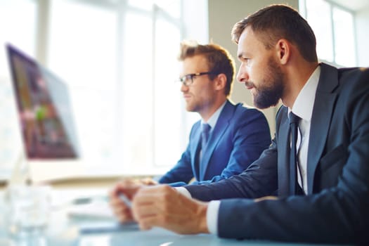 Young businessman looking at computer monitor with colleague near by