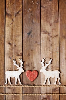Two reindeers on ropes and red heart between them on wooden background