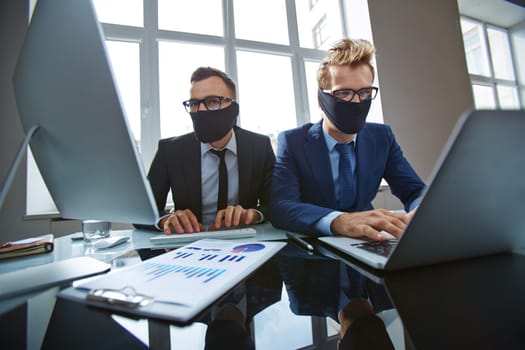 Two businessmen with their mouths tied up typing in office