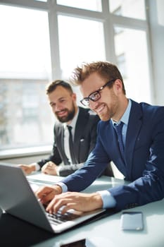 Smiling businessman browsing on laptop with co-worker on background