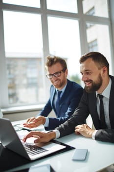 Young businessman pointing at laptop display while consulting his colleague at meeting