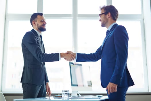 Confident businessmen handshaking over workplace in office