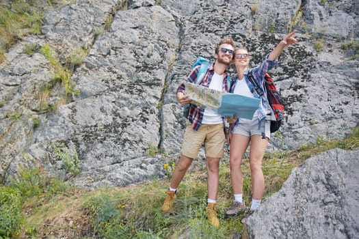 Active young couple with map looking at distant place while standing by rock