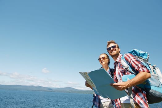 Cheerful hikers with map enjoying their trip on background of sky and sea