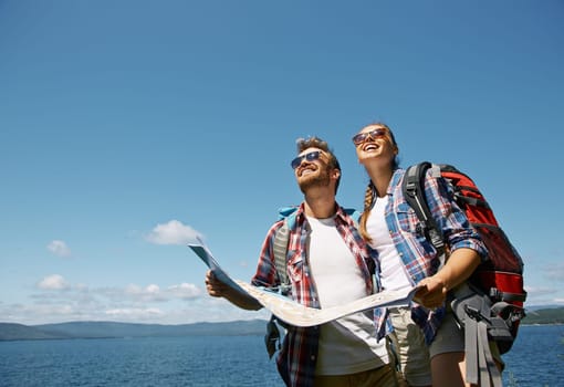 Cheerful hikers with map looking upwards against blue sky
