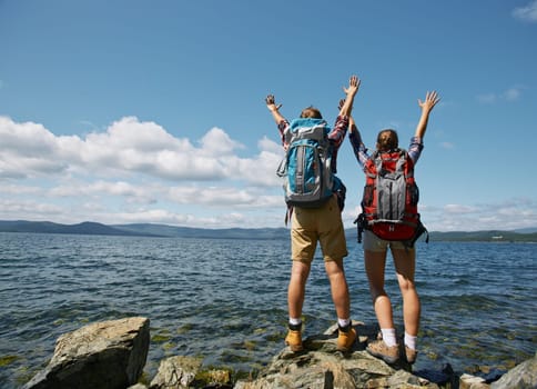 Couple of travelers with raised arms enjoying summer vacation by the sea