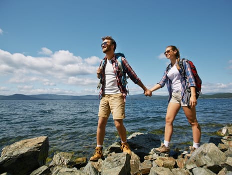 Happy couple holding by hands while walking on rocks by the seaside