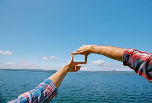 Human hands making frame against blue sky by the seaside