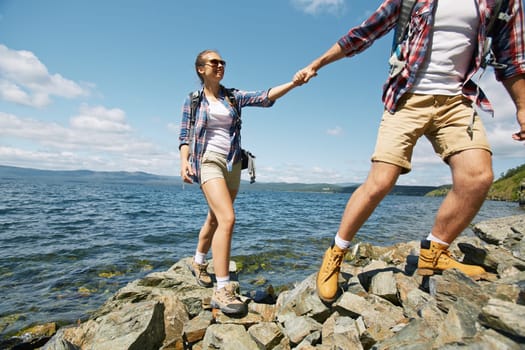 Happy girlfriend holding by her boyfriend hand while climbing on rocks