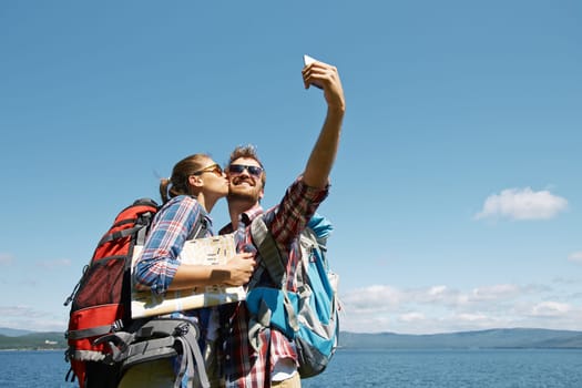 Happy man making selfie during trip while his girlfriend kissing him