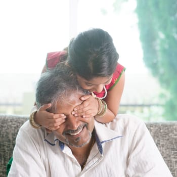 Happy Indian family at home. Asian girl surprising her father by covering daddy eyes. Parent and child indoor lifestyle.