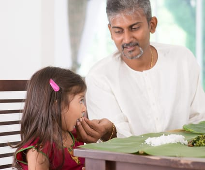 Indian family dining at home. Candid photo of India people eating rice with hands. Parent feeding child.