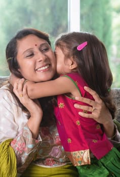 Happy Mother Day. Indian family at home. Asian girl kissing her mother, sitting on sofa. Parent and child indoor lifestyle.