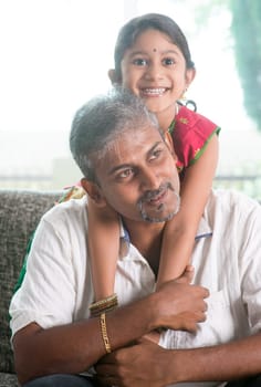 Happy Indian family at home. Asian father piggyback her daughter, sitting on sofa. Parent and child indoor lifestyle.