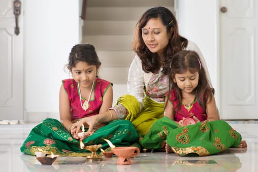 Indian family in traditional sari lighting oil lamp and celebrating Diwali, fesitval of lights at home.